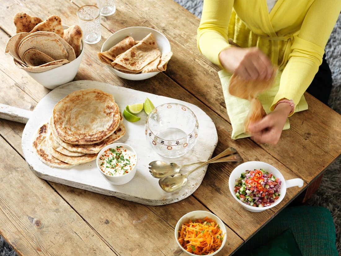 Fladenbrot und verschiedene Beilagen auf rustikalem Holztisch (Indien)