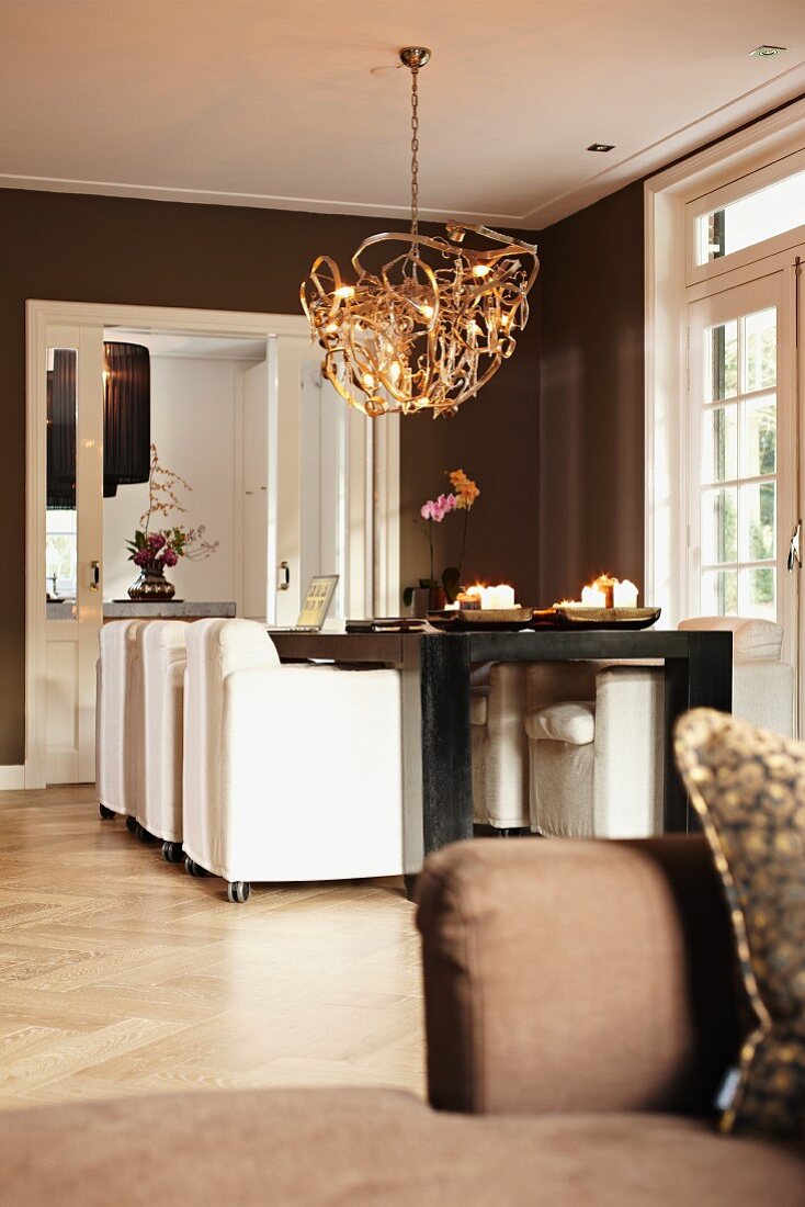 Moderne Hängeleuchte über Esstisch und weissen Polstersesseln in braun getöntem Wohnraum mit traditionellem Flair