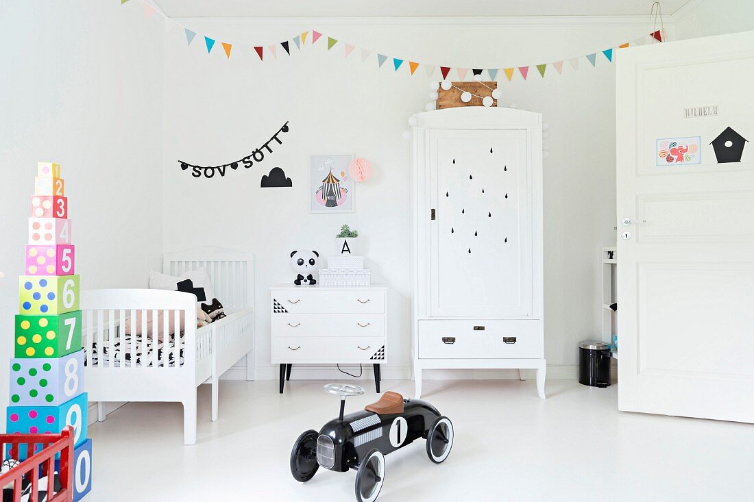 Black, retro-style toy car in white nursery with colourful bunting and stacked toy blocks