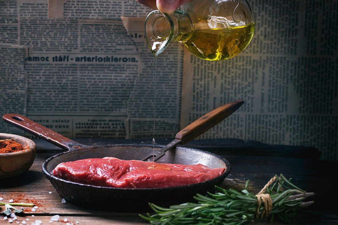 A raw beef steak being drizzled with olive oil