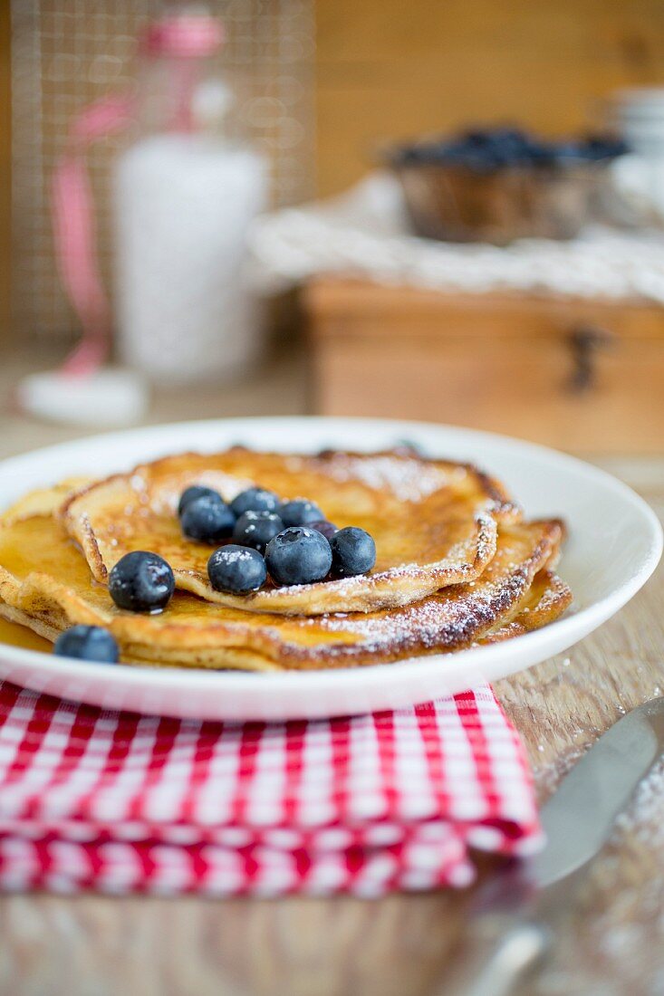 A stack of pancakes with icing sugar and blueberries