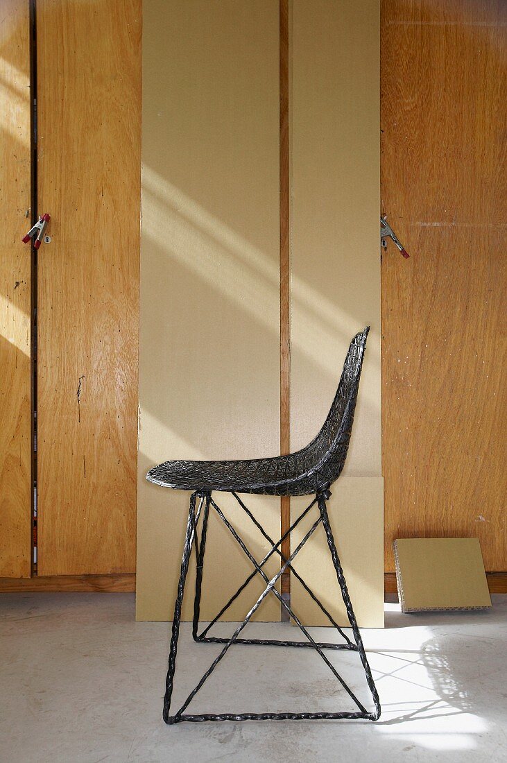 Carbon Chair by Moooi in front of planks leaning against fitted cupboards