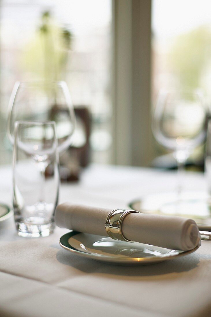 A fabric napkin on a plate and empty glasses on a table in a restaurant