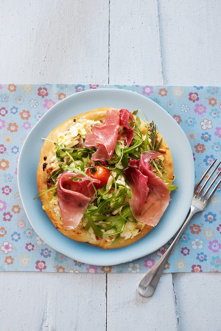 Pizza with ham, rocket, tomatoes and pine nuts
