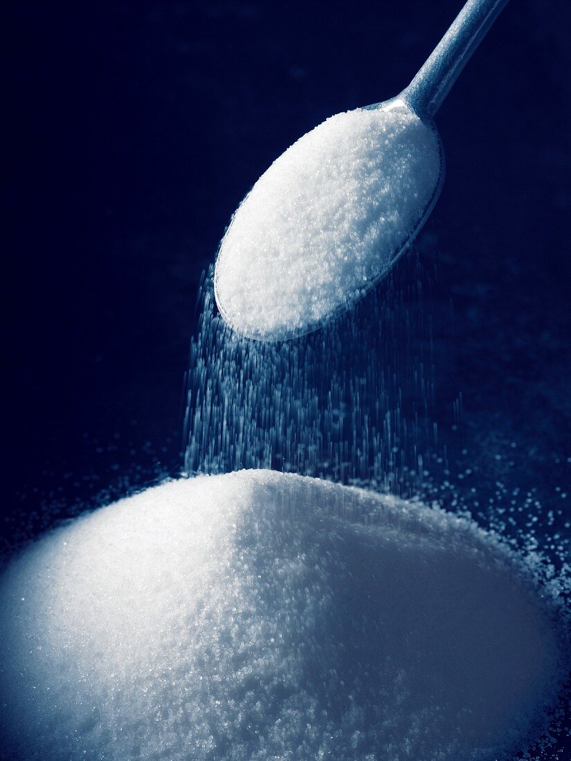 Sugar being sprinkled from a spoon onto a pile of sugar