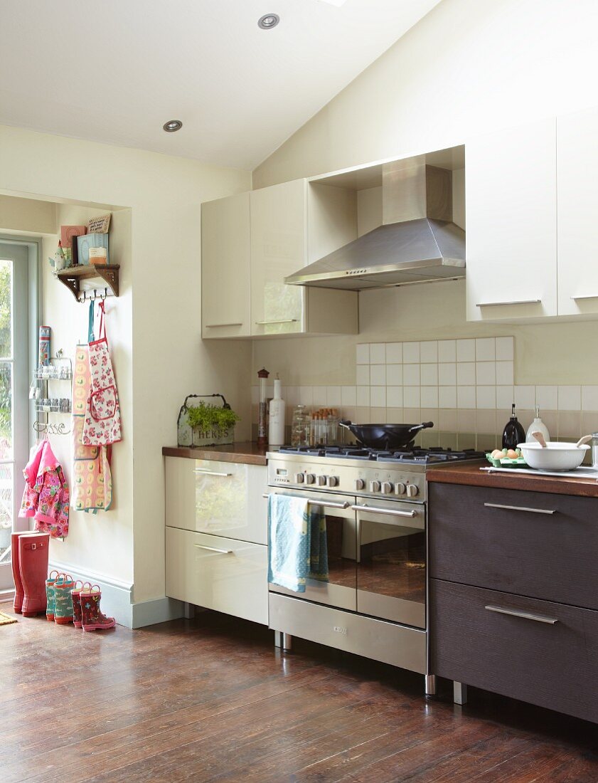 Stainless steel cooker element between light and dark base unit in simple fitted kitchen with access to garden