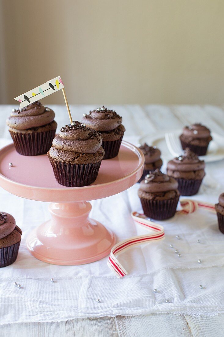 Chocolate cupcakes with chocolate cream and chocolate sprinkles on a pink cake stand