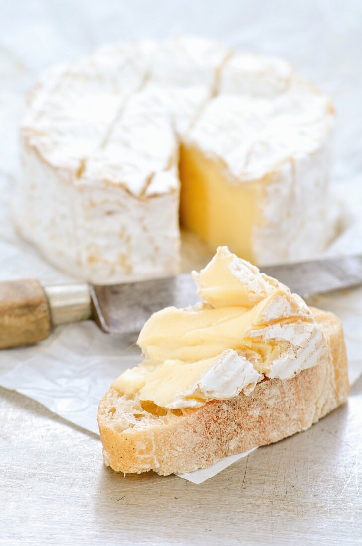 A slice of bread topped Camembert with a sliced Camembert in the background