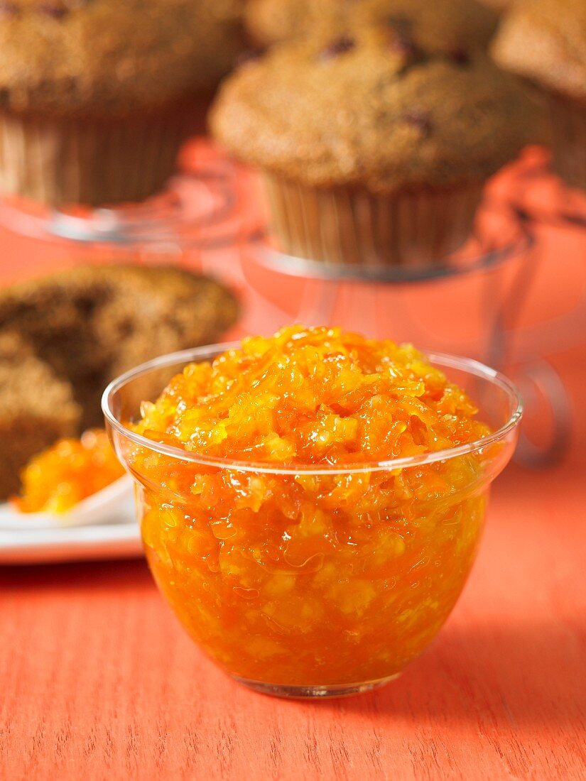 Carrot and pineapple jam in a glass bowl with muffins in the background