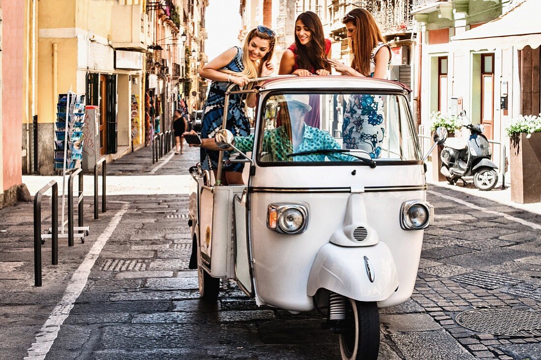 Drei junge Frauen stehen in offenem nostalgischem Taxi in Cagliari (Sardinien, Italien)