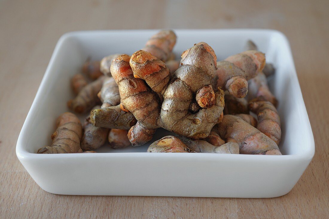 Fresh turmeric roots in a porcelain dish