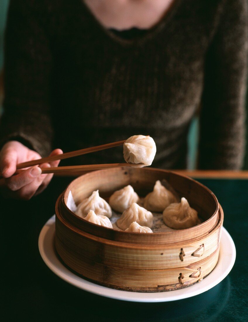 A woman with wooden chopsticks holding a steamed dumpling