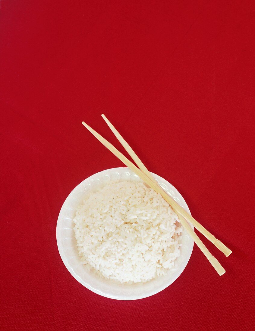 Reisschüssel und Essstäbchen auf rotem Untergrund