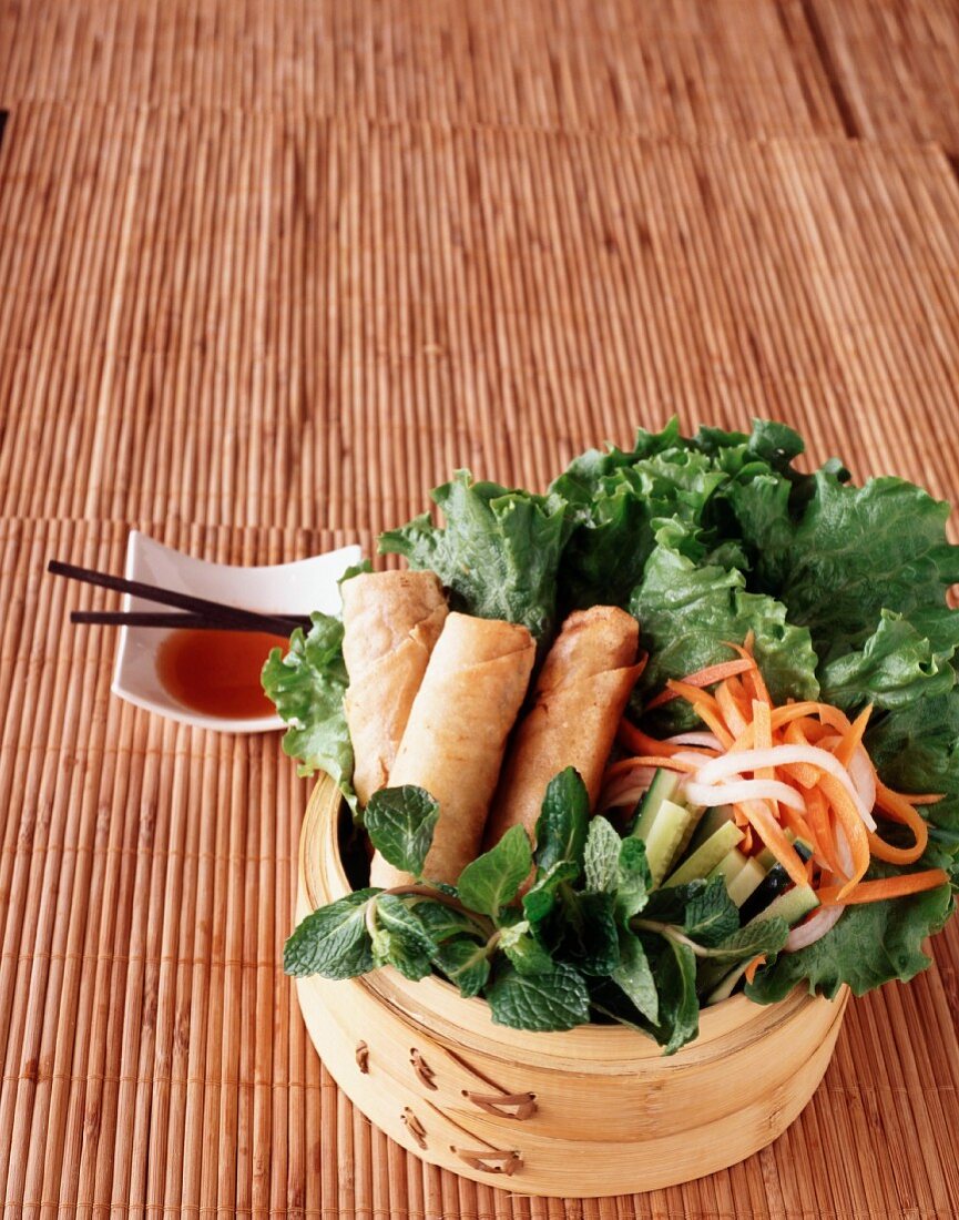 Vegetarische Frühlingsrollen auf Salat mit Daikon-Rettich und Karotten; dazu süsse Chilisauce