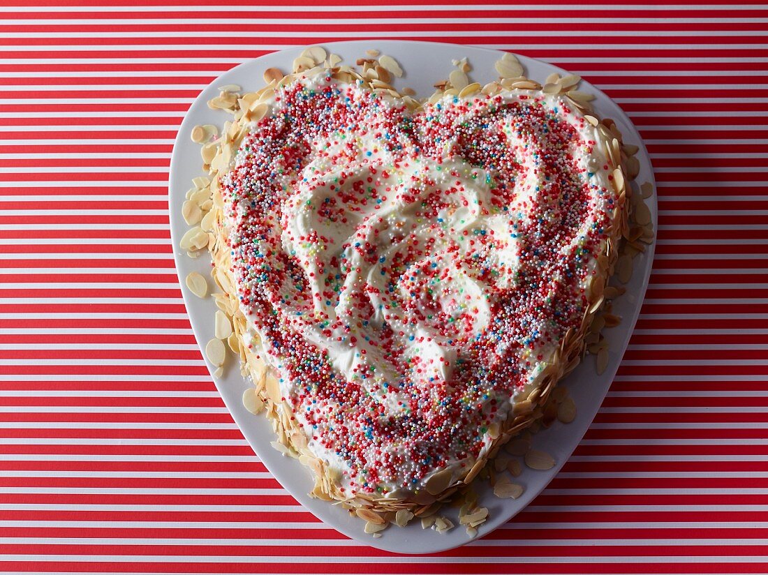 A heart-shaped cake decorated with colourful sprinkles and flaked almonds