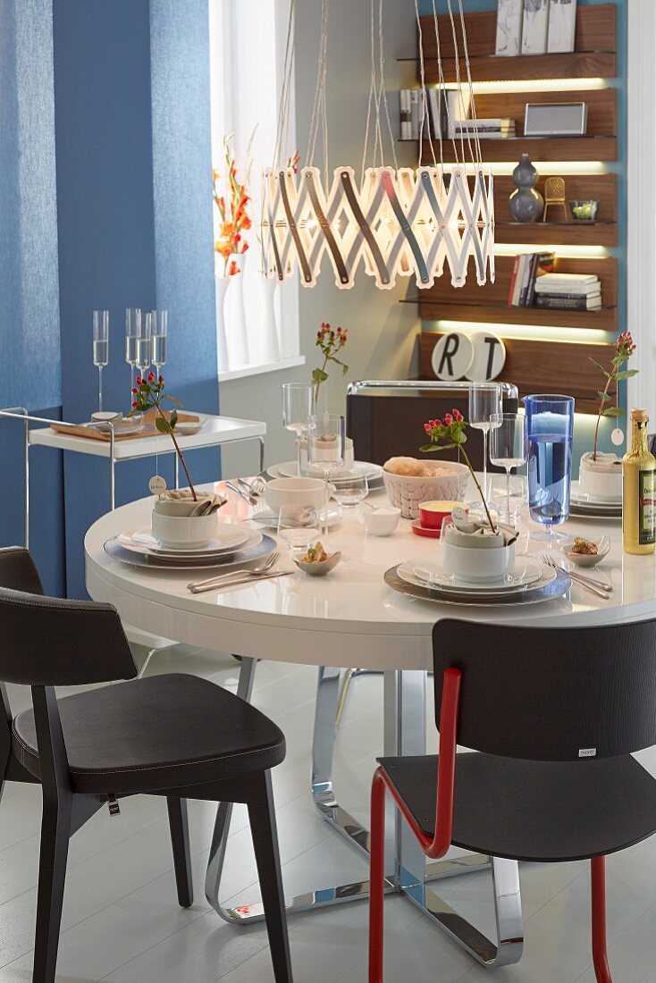 Various black chairs around a festively laid table with a concertina-style pendant lamp hanging above it