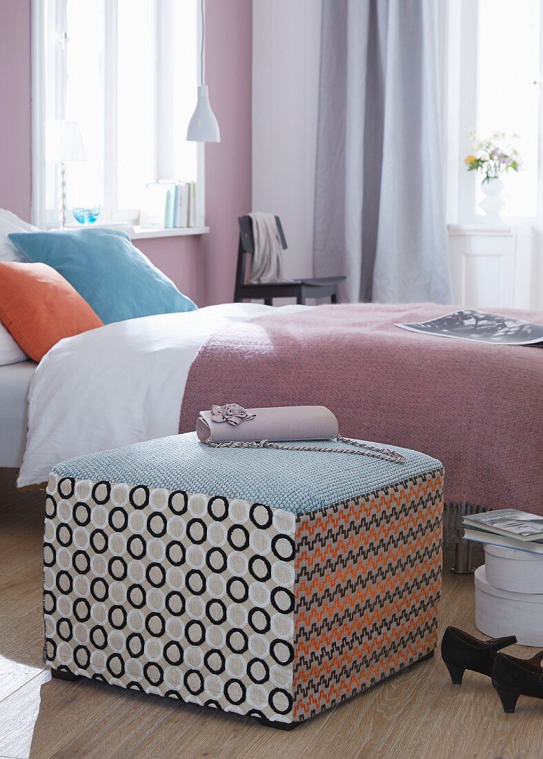 A patchwork pouffe as a bedside table or a seat next to a bed with a lilac bedspread