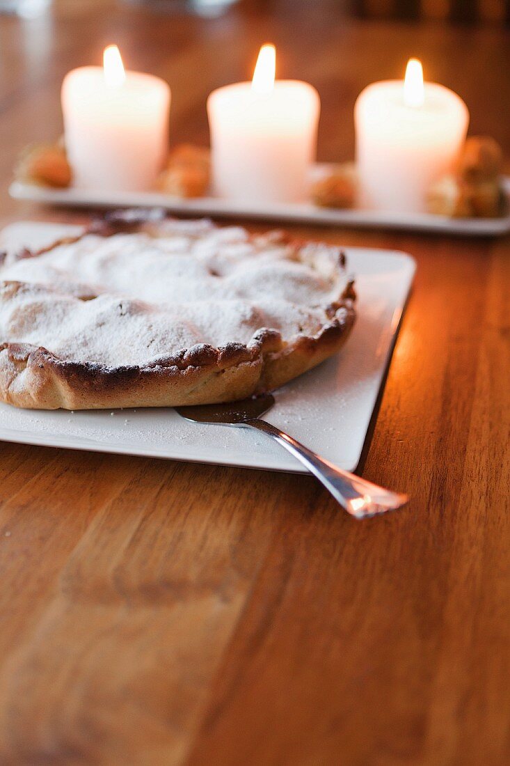 Kuchen unter Puderzuckerdecke, im Hintergrund brennende Kerzen