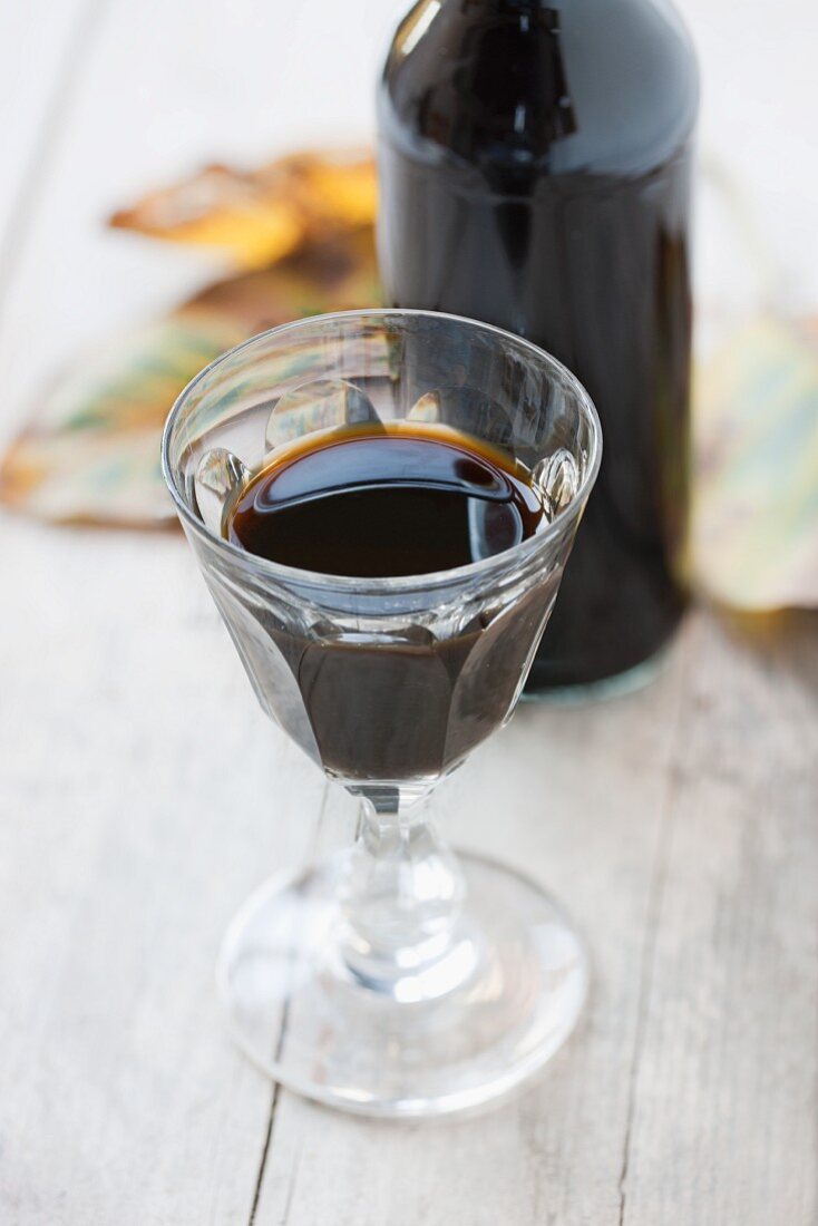 A glass and a bottle of homemade nut wine (vin de noix) with autumnal walnut leaves