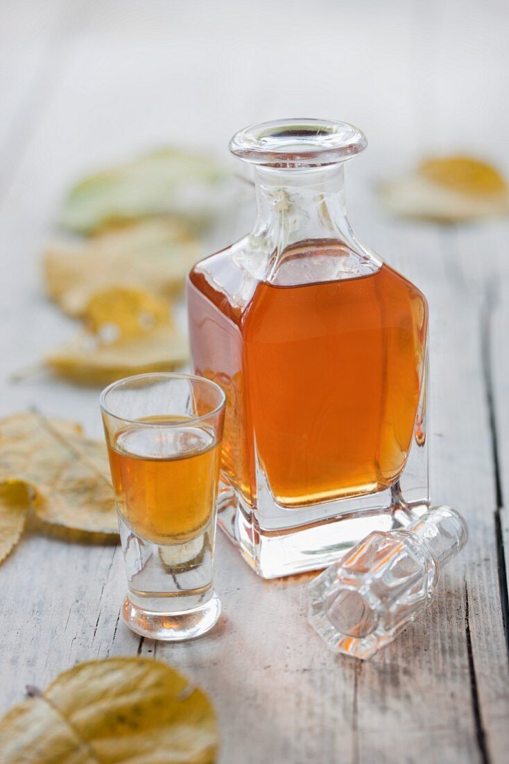 A small glass of homemade damson stone liqueur on a wooden surface next to autumnal damson leaves