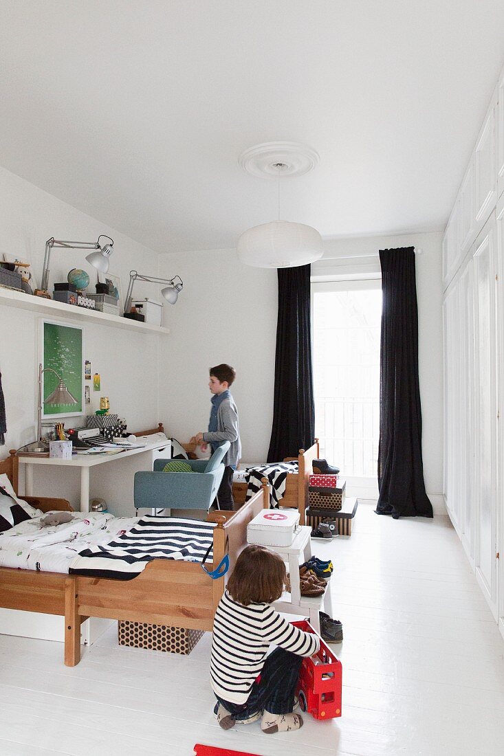 Siblings' bedroom with wooden beds, desk and long, black curtains on window