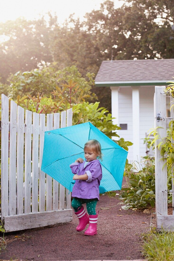 Little girl walking in garden carrying umbrella
