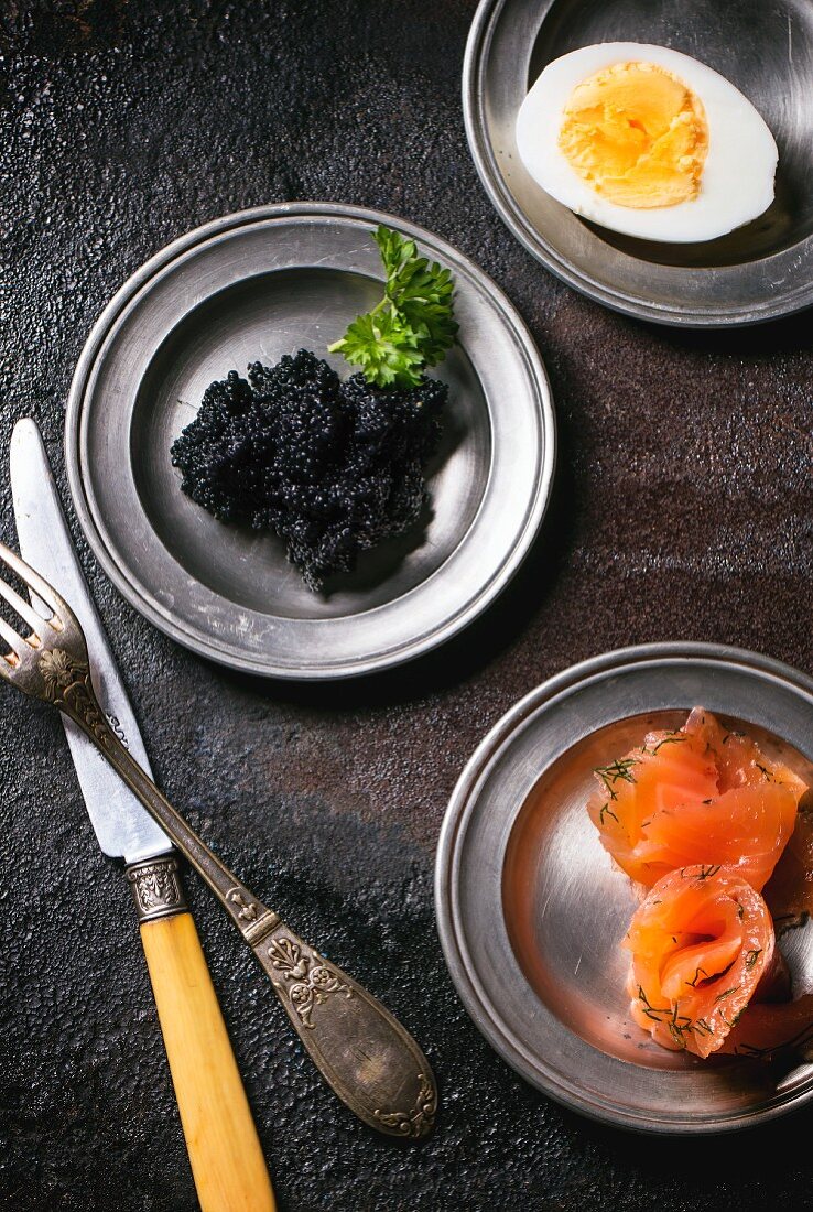 Schwarzer Kaviar, Räucherlachs und hartgekochtes Ei auf drei Zinntellern