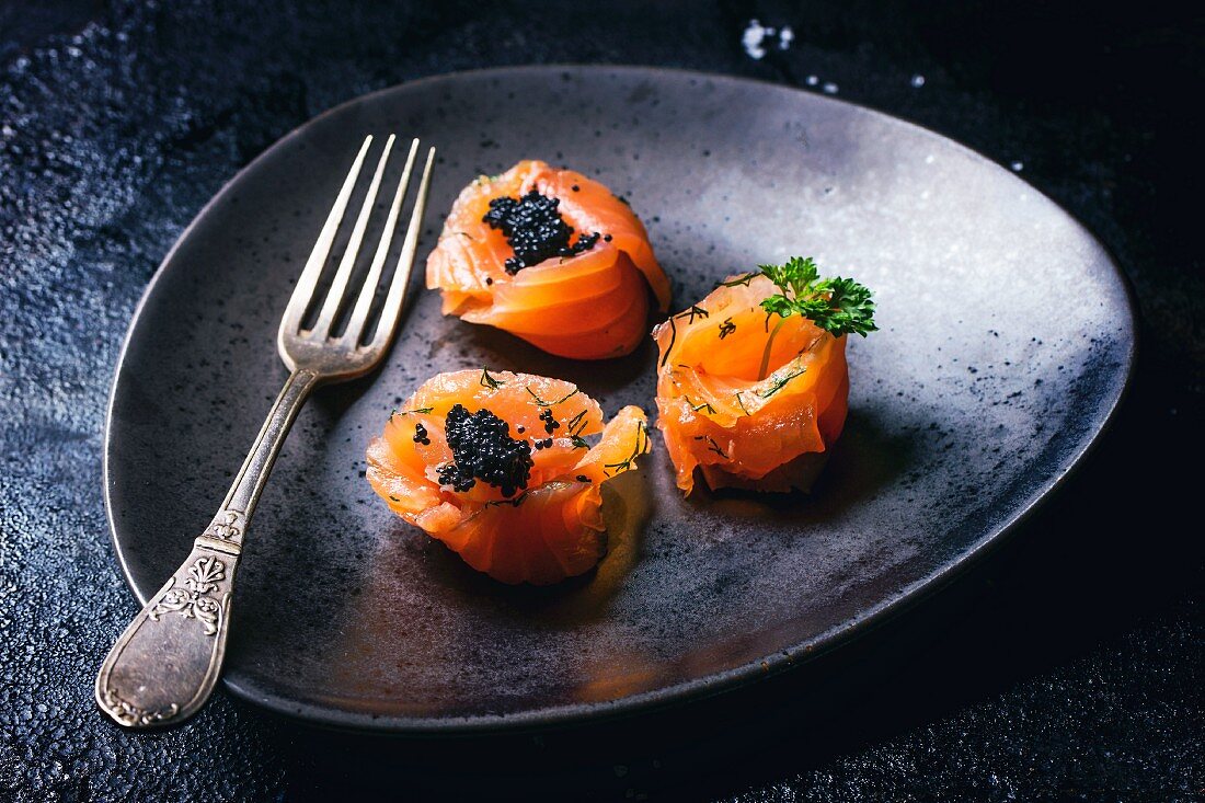 Lachsröllchen mit schwarzem Kaviar auf Teller mit Gabel