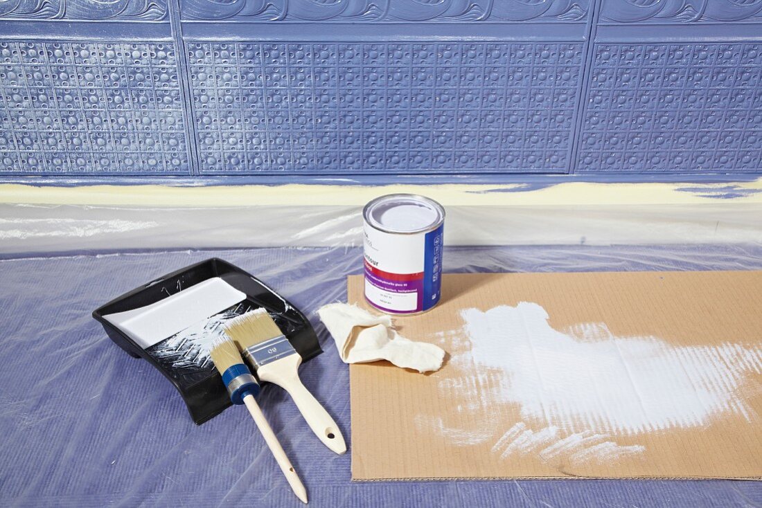 Malerutensilien auf Boden vor Lincrusta (Strukturtapete aus linoleumähnlichem Material) an Wand, blau bemalt