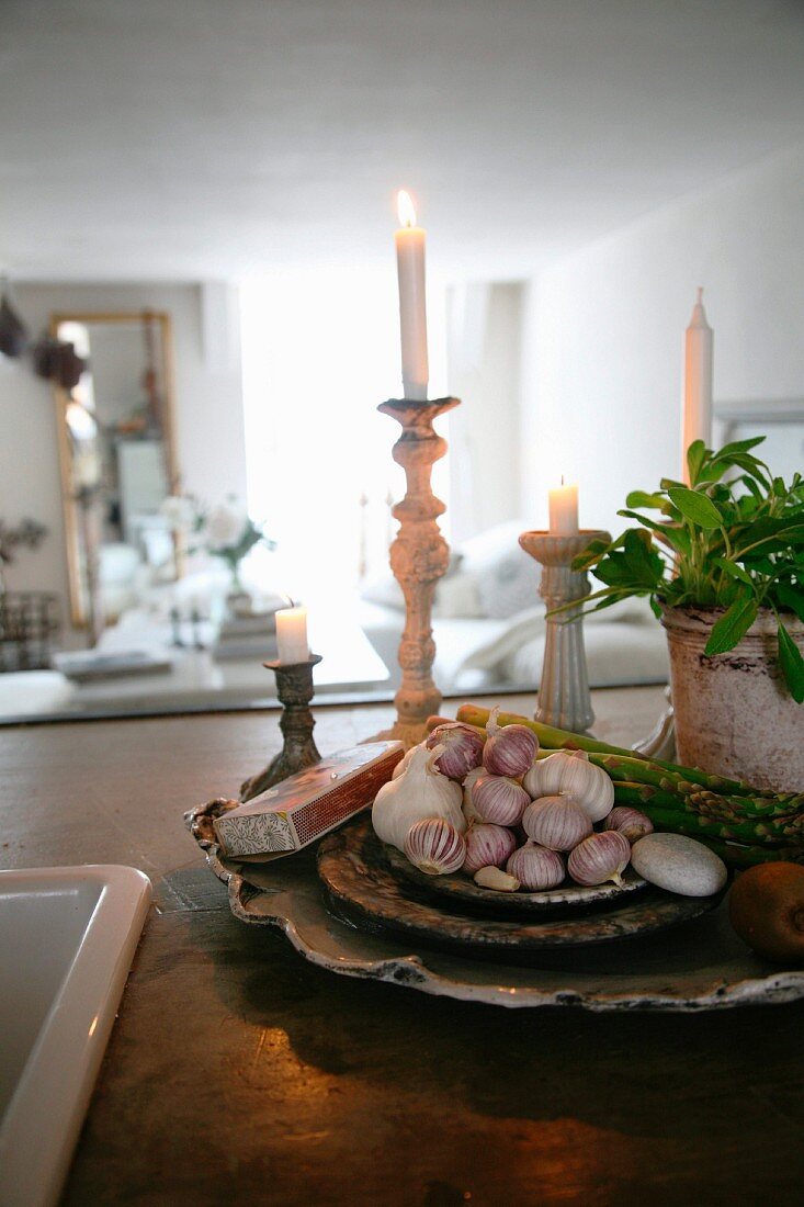 Bulbs of garlic on stacked dishes in front of lit candles in candlesticks