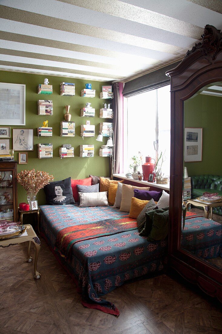 Couch with many scatter cushions in living room with green accent wall and green and white striped ceiling