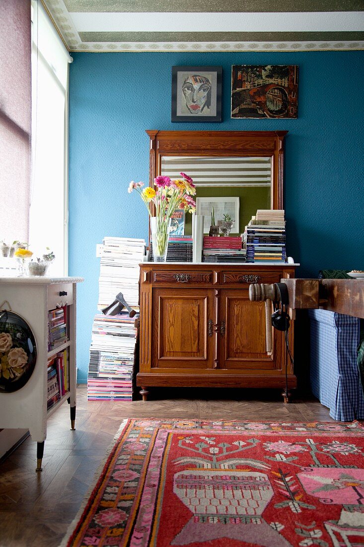 Stacked magazines on top of antique cabinet with mirror against blue wall