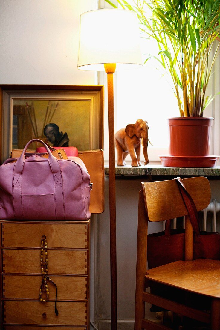 Standard lamp with white lampshade, pink handbag on chest of drawers and wooden chair