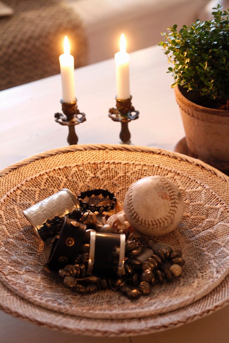 Beaded jewellery and old baseball in flat basket next to lit candles in vintage candlesticks