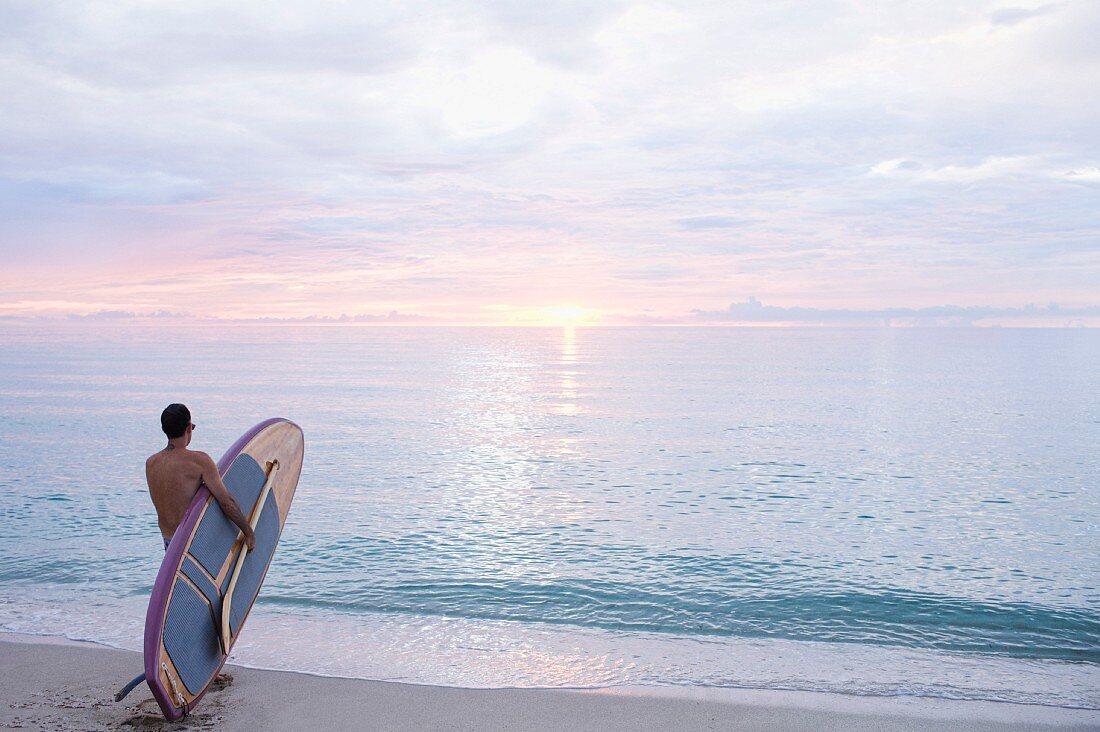 Mann mit Paddelbrett im Morgenlicht aufs Meer blickend