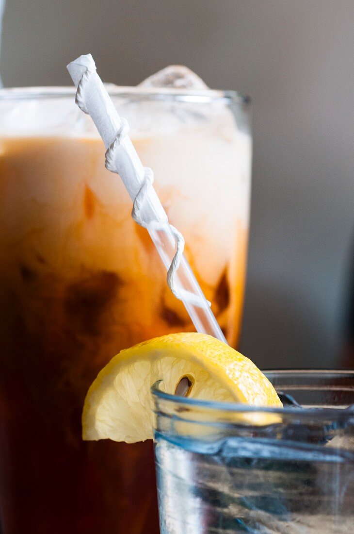 Wasserglas mit Strohhalm und Zitronenscheibe vor einem Milchshake