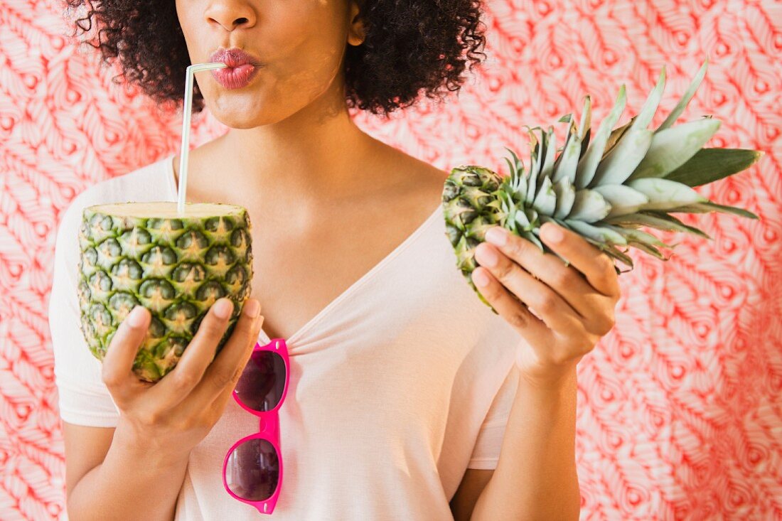 A young woman drinking cold juice from a pineapple