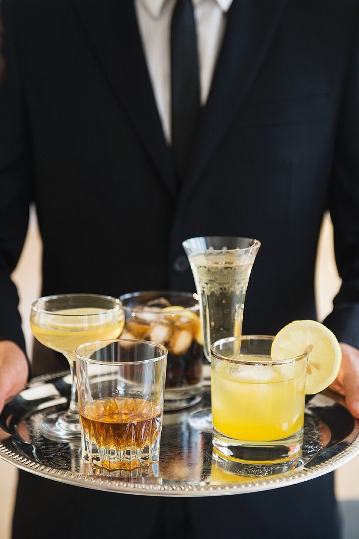 A young waiter serving various drinks from a silver tray