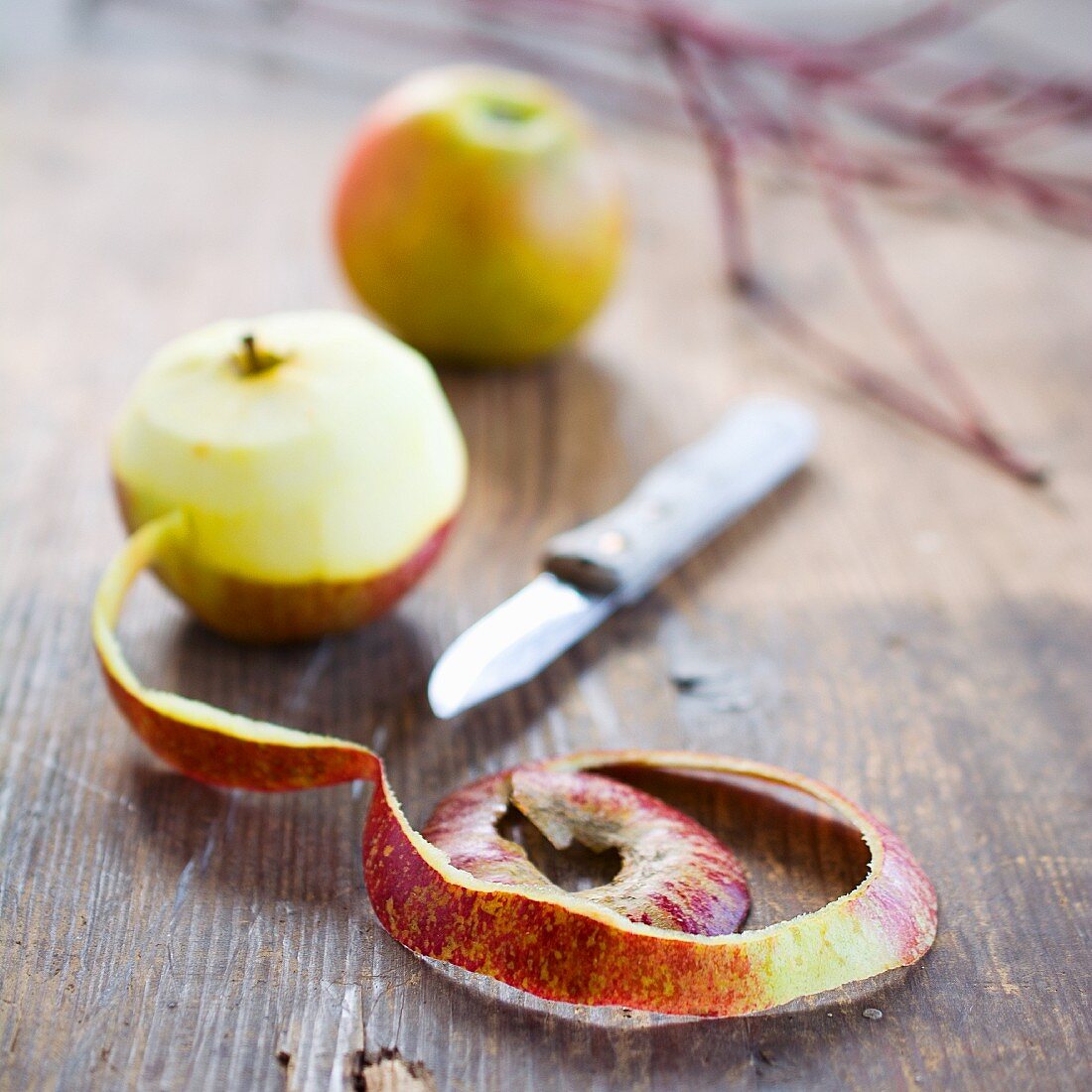 Apples, one partially peeled, on a wooden table
