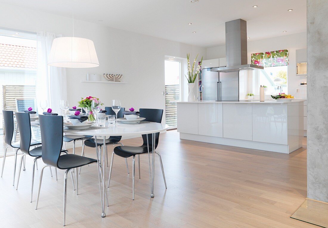 Festively set oval table and black chairs in light-flooded interior with open-plan designer kitchen