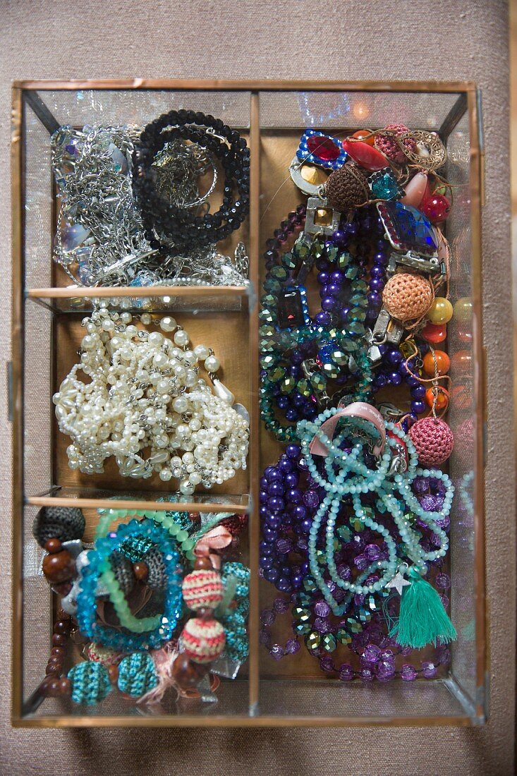 Various bead necklaces in open-topped, glass jewellery box