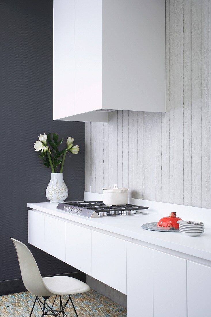 Minimalist kitchen counter with classic chair in front of gas hob and extractor hood on exposed concrete wall