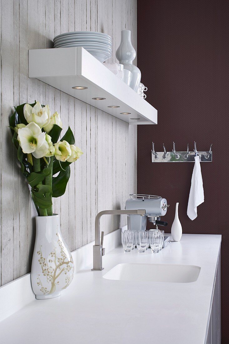 Corian worksurface with integrated sink below floating shelf with downlights on exposed concrete wall in minimalist designer kitchen