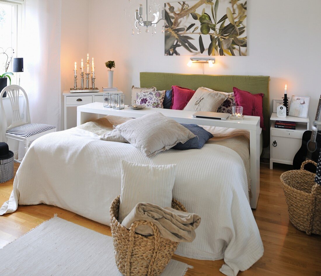 Narrow over-bed table above bed with many scatter cushions, lit candles and woven baskets