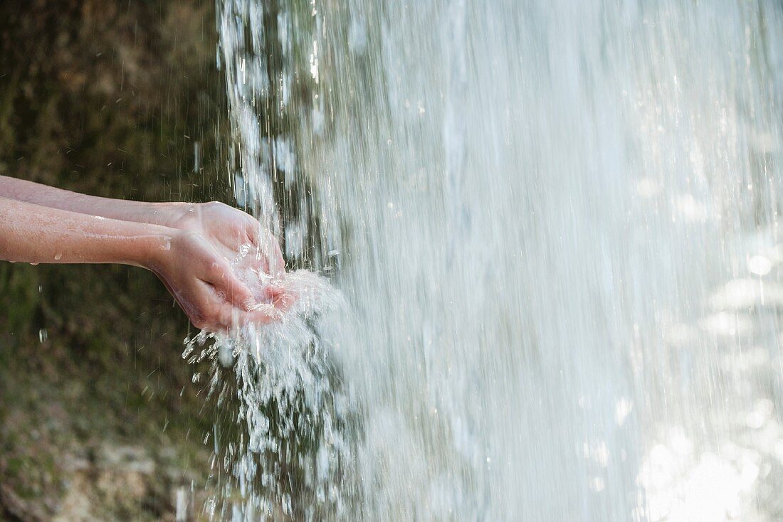 A person holding their hands under a waterfall
