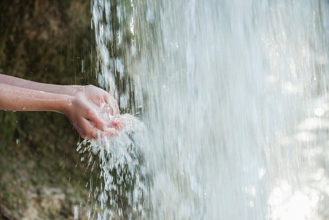 Person hält Hände unter Wasserfall