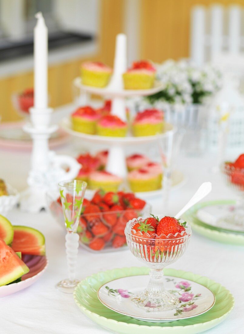 Gedeckter Tisch mit Erdbeern, im Hintergrund Kerzen und Etagere mit Kleingebäck