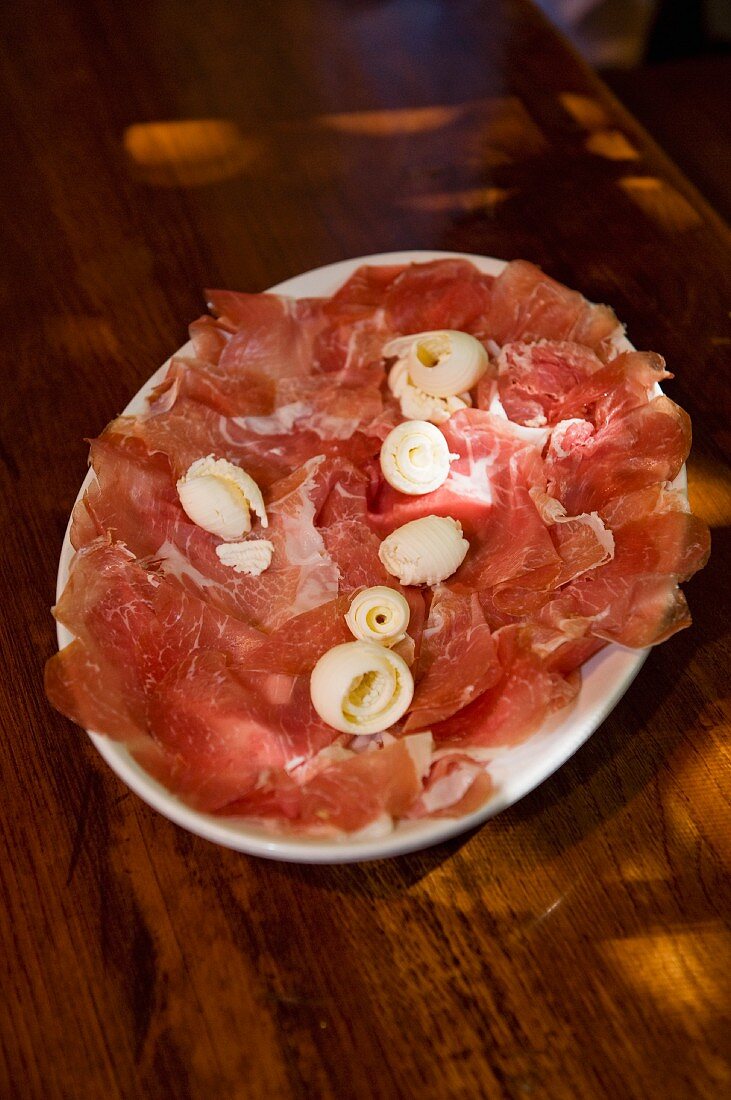 Italian raw ham, finely sliced and arranged on a platter with curls of butter
