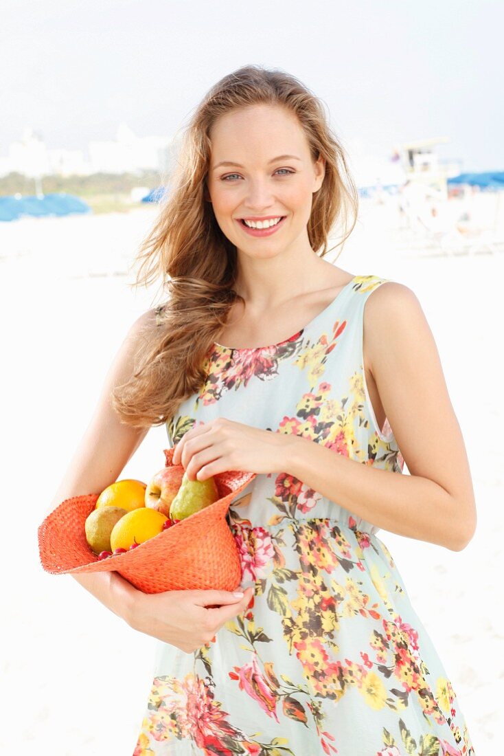 A young woman wearing a summer dress holding a hat filled with fruit