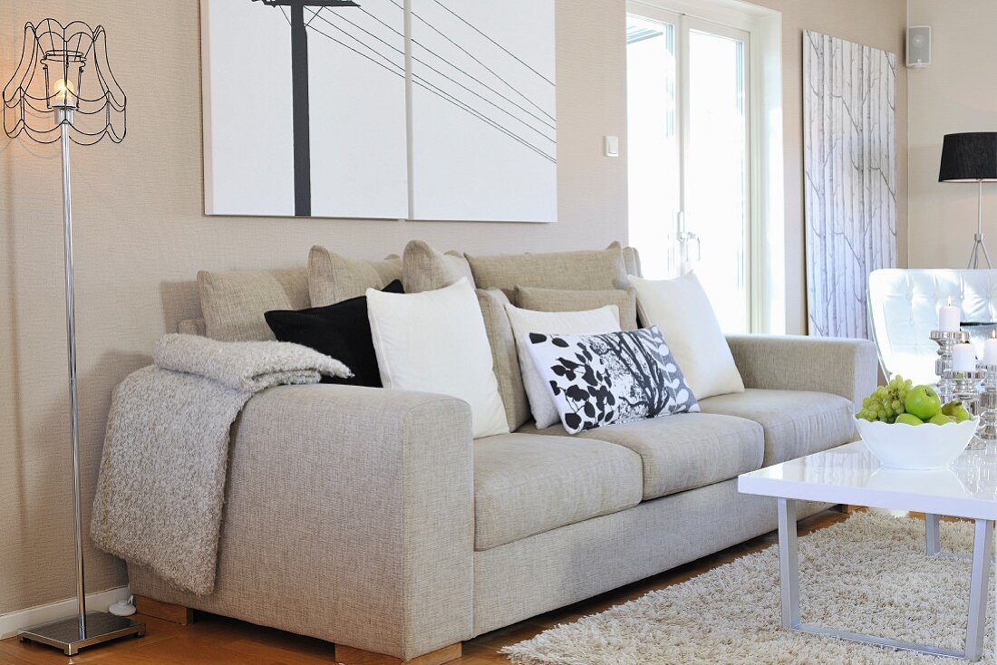 Ecru sofa with scatter cushions next to retro standard lamp, modern coffee table and rug in contemporary living room
